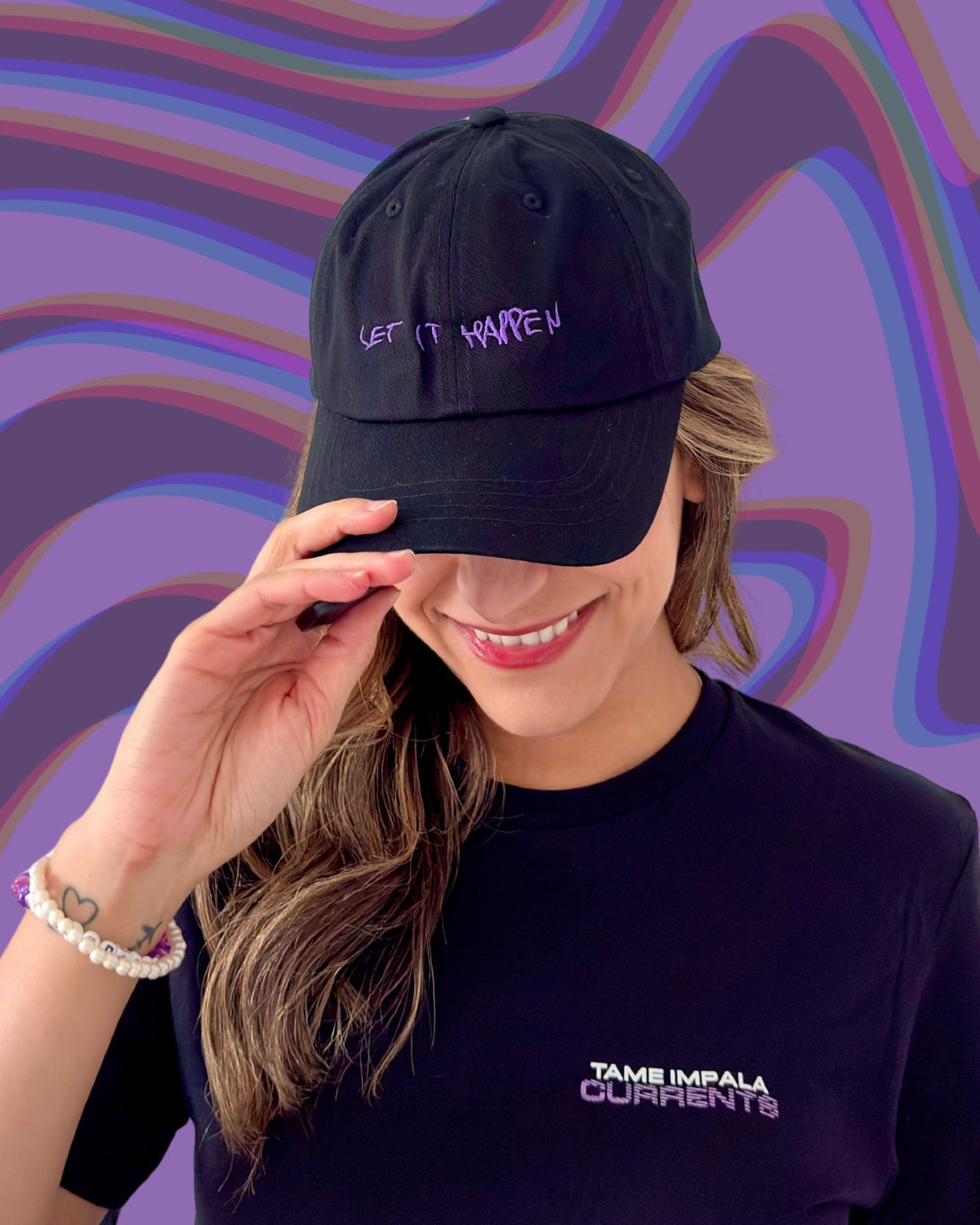 Model is wearing a black cap with "Let It Happen" in Kevin Parker's handwritten purple text and wearing a t-shirt with text "Tame Impala Currents", against a colorful wavy background