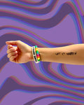 Model wearing a "Let it Happen" temporary tattoo on arm with a colorful bracelet on a multicolored wavy background