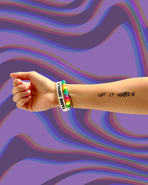 Model wearing a "Let it Happen" temporary tattoo on arm with a colorful bracelet on a multicolored wavy background