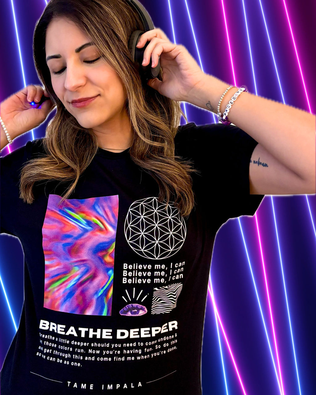 A woman wearing a black Tame Impala graphic t-shirt with psychedelic and geometric designs, set against a vibrant background of purple and pink neon vertical lines.