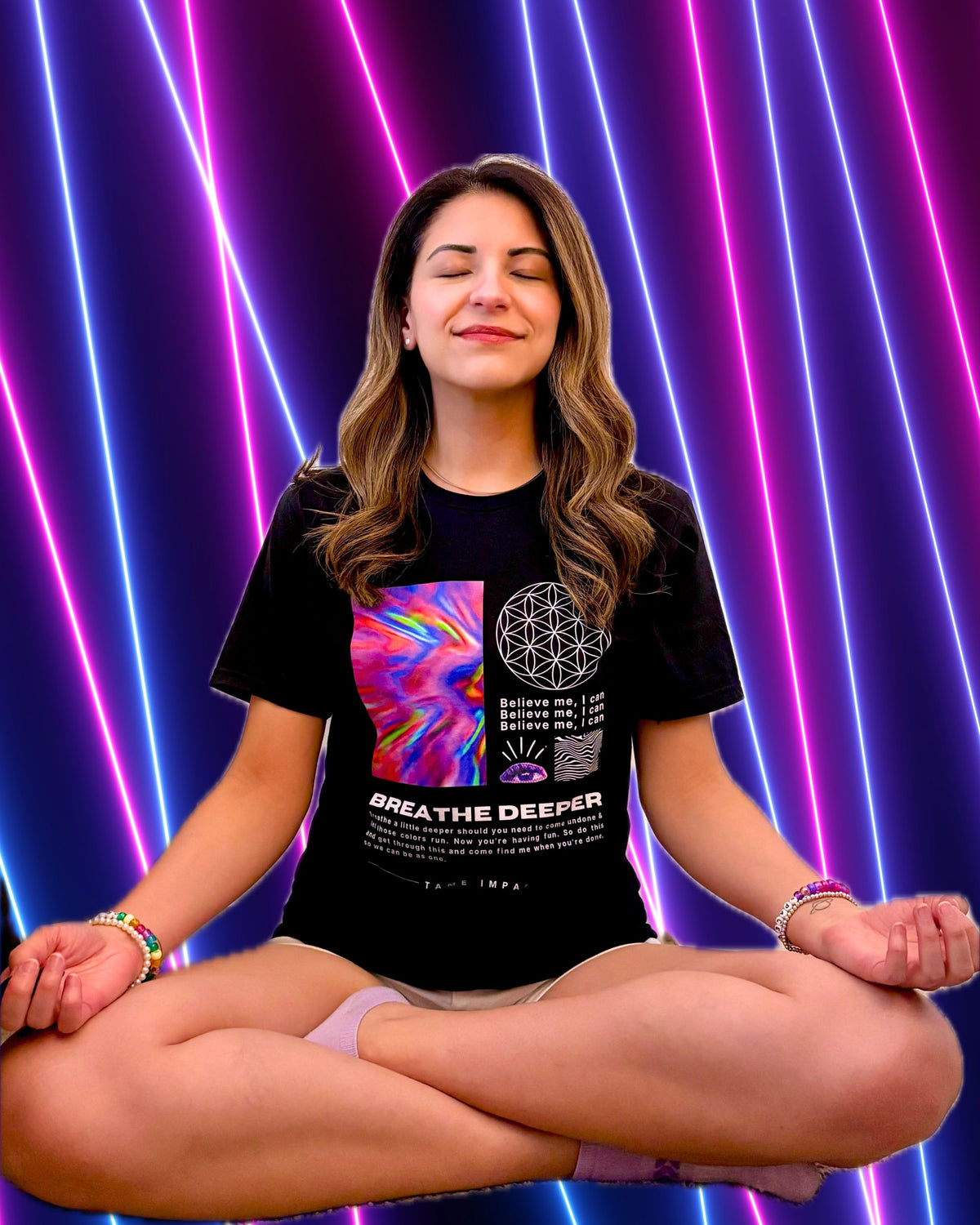 A woman meditating in a lotus position wearing a black Tame Impala graphic t-shirt with a colorful abstract print and the text 'BREATHE DEEPER'. She is posed against a vibrant background of vertical neon pink, purple, and blue light tubes.