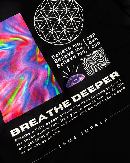 Close-up of a black graphic T-shirt featuring white text reading 'BREATHE DEEPER' and 'TAME IMPALA,' a white geometric flower symbol, a colorful iridescent abstract panel, and a purple eye illustration.