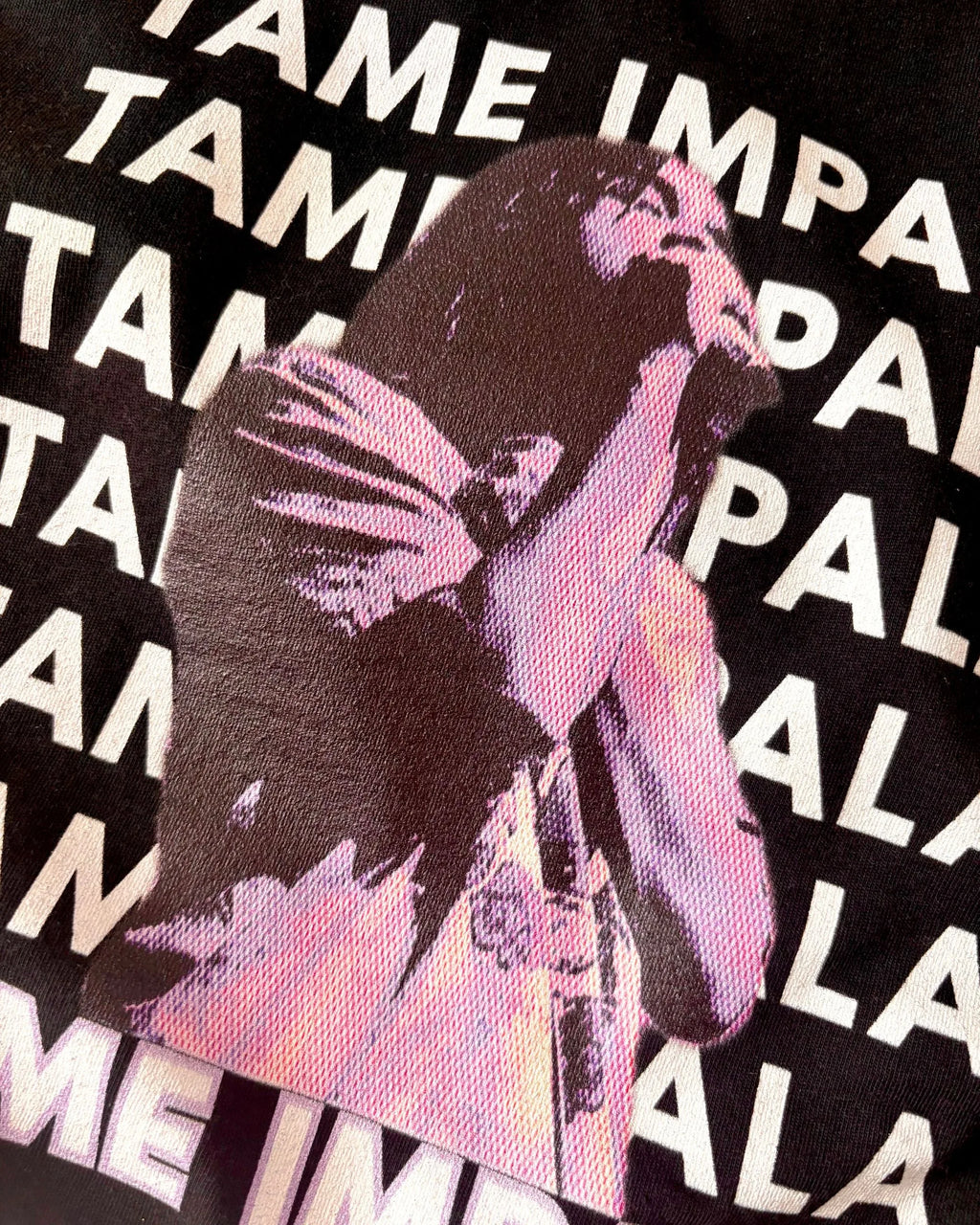 Close up of the black Tame Impala T-shirt featuring Kevin Parker in a purple filter and repeating Tame Impala text