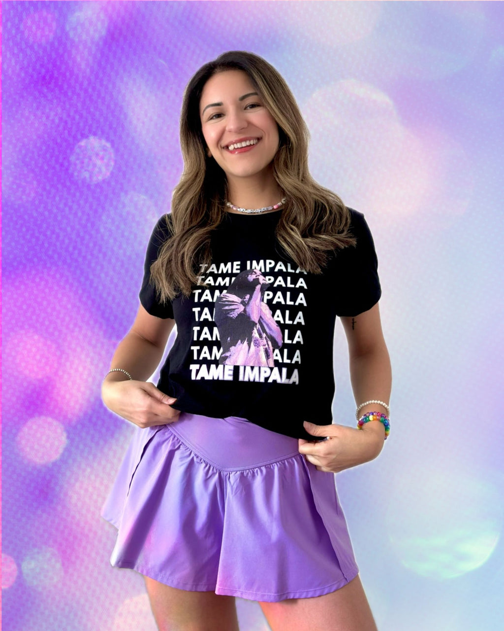 Woman wearing a black t-shirt with 'Tame Impala' repeating text design and a photo of Kevin Parker with a purple filter wearing a purple skort