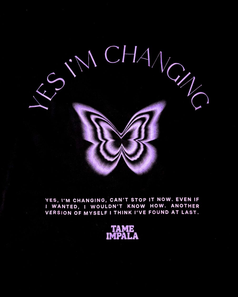 A black graphic print featuring a stylized purple butterfly in the center, with the words 'YES I'M CHANGING' arched above it and additional text below reading 'YES, I'M CHANGING, CAN'T STOP IT NOW, EVEN IF I WANTED, I WOULDN'T KNOW HOW. ANOTHER VERSION OF MYSELF I THINK I'VE FOUND AT LAST.